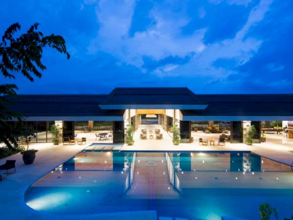 Modern hotel at dusk with a lit outdoor swimming pool and loungers under a vivid blue sky.