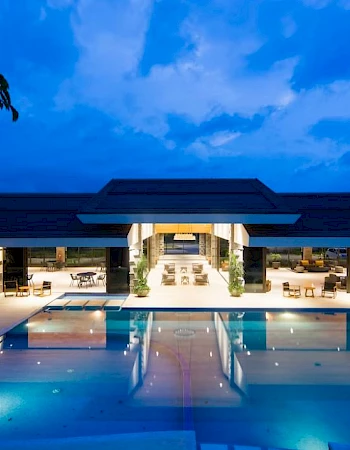 A modern hotel courtyard with a lit outdoor swimming pool and lounge chairs under a dramatic blue evening sky.