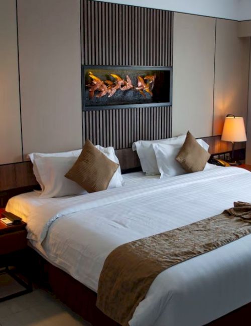 A modern hotel room with a made bed, bedside lamps, and a wall fireplace beside drawn curtains.