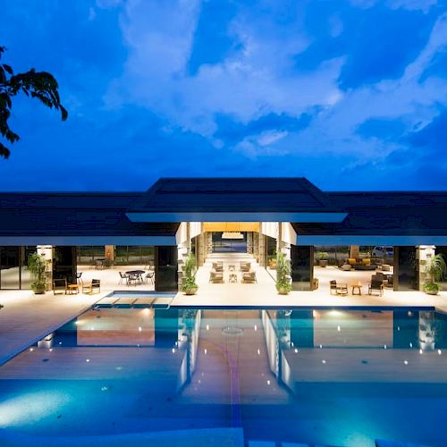 A modern resort pool at dusk with lounge chairs and a sleek building under a bright blue sky.