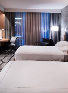A modern hotel room with two neatly made beds, a wall TV, and curtains framing large windows.