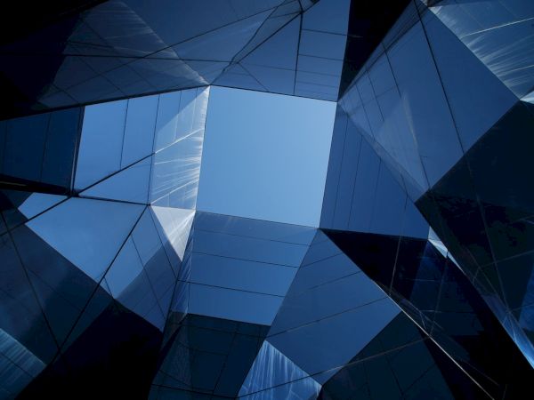 A blue, geometric glass-and-steel building facade shot from below, with sharp angles and reflections.