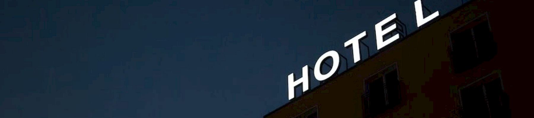 A tall building with a glowing “HOTEL” sign on its rooftop under a dark evening sky.