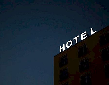 A tall building with a glowing “HOTEL” sign on its rooftop under a dark evening sky.