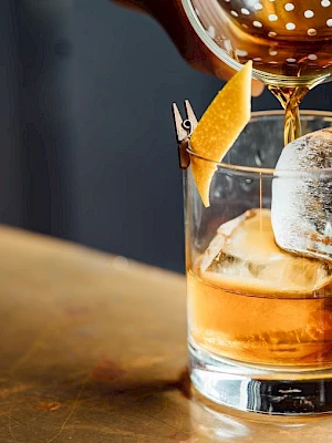 A bar cocktail in a rocks glass with amber liquor, ice, and a pineapple wedge garnish on top.