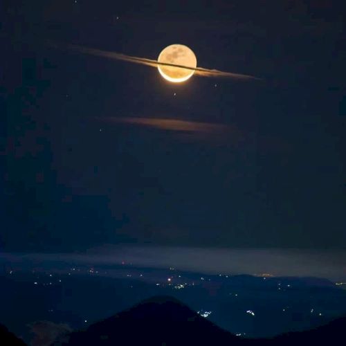 A bright moon hangs over dark mountains as a glowing ring-like object passes across it in a night sky.