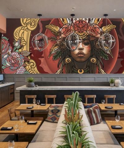 A stylish restaurant with a bold mural of a woman in ornate headdress on the back wall, wooden tables, plants, and modern decor.