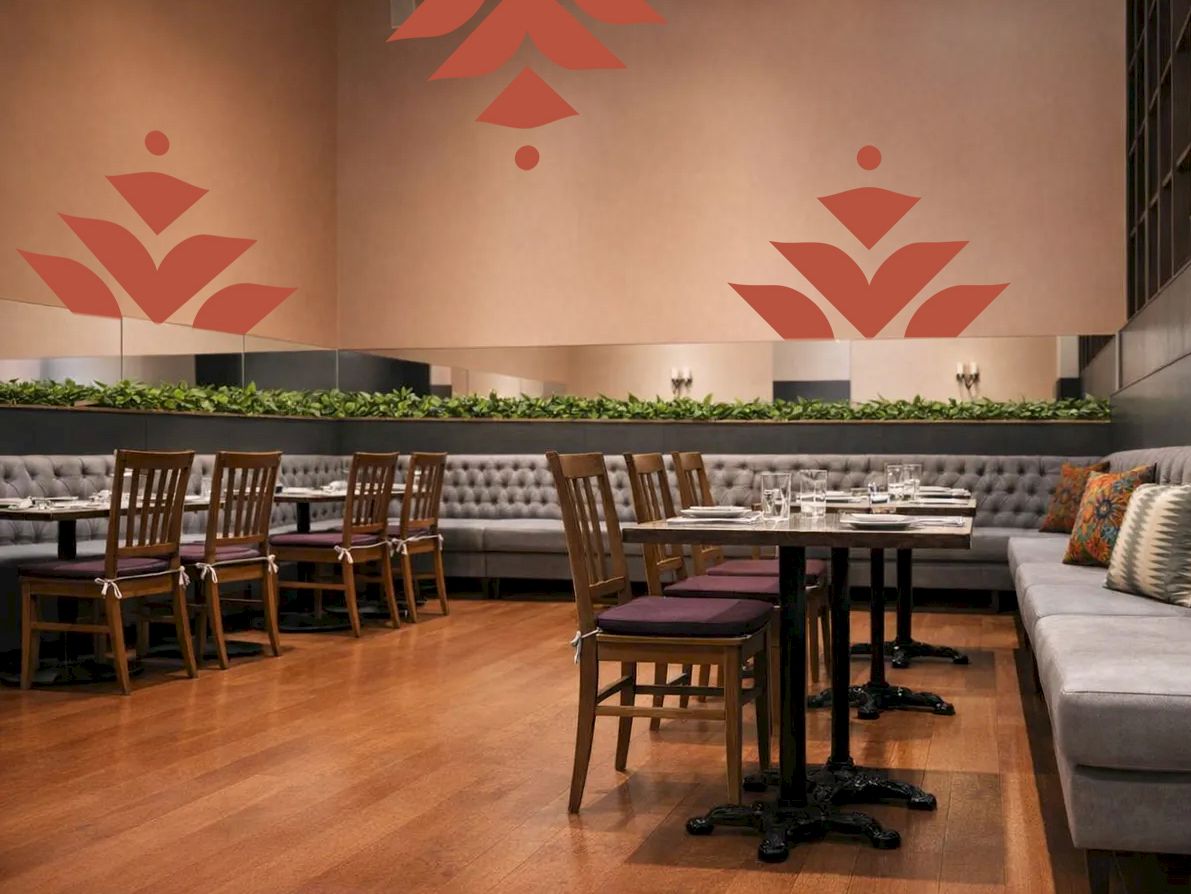 A cozy restaurant with wooden floors, cushioned seating along the walls, several tables and chairs, and decorative red wall art patterns.