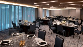 A modern banquet room set with round tables, fine glassware, candles, and place settings for a formal dinner.