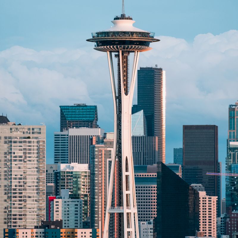 Seattle&rsquo;s iconic Space Needle rises above downtown under a blue sky, its observation deck perched high among skyscrapers.