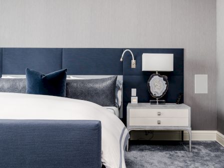 A modern hotel bedroom with a bed, blue pillows, and a nightstand holding a lamp, decorative geode, and a remote control.