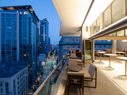 A modern high-rise balcony with lounge seating and views down a city street lined with tall buildings.