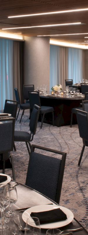 An elegant banquet hall set with neatly arranged round tables, place settings, and soft lighting under modern ceiling fixtures.