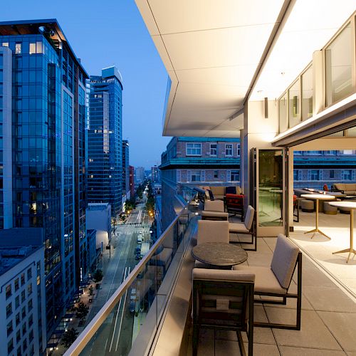A modern apartment high-rise balcony overlooks a city street and skyscrapers as dusk light fills the terrace.